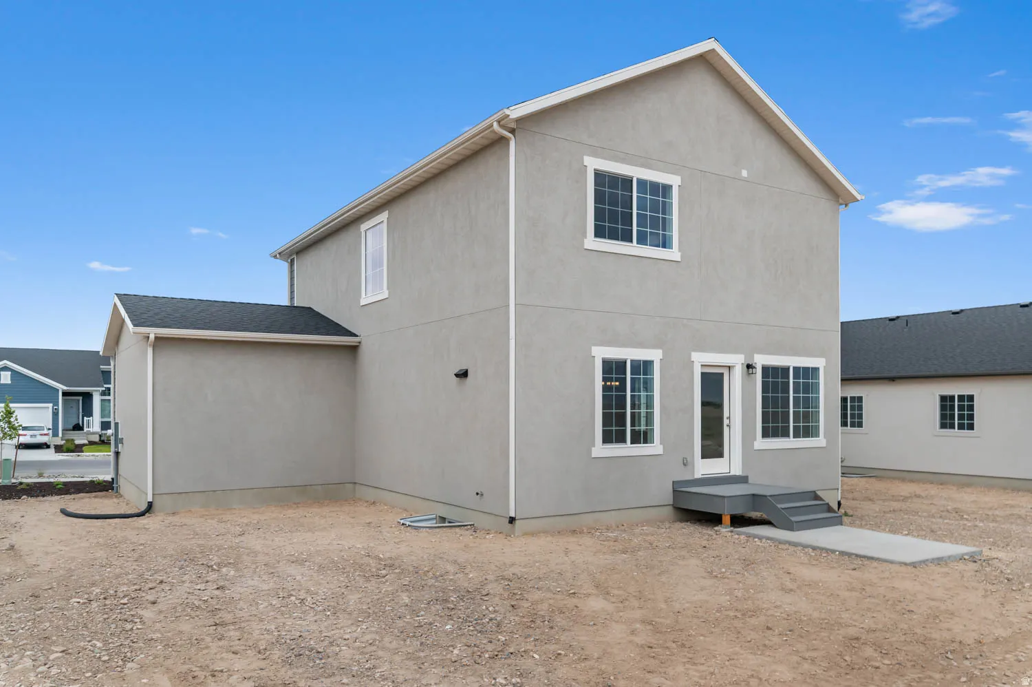 Two-story stucco exterior featuring multiple windows with white trim, a rear entry door, and a small deck with steps leading to a concrete path