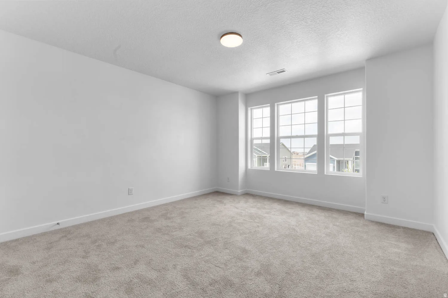 Spacious room featuring three large windows, light gray carpeting, neutral wall paint, and a flush-mount ceiling light fixture