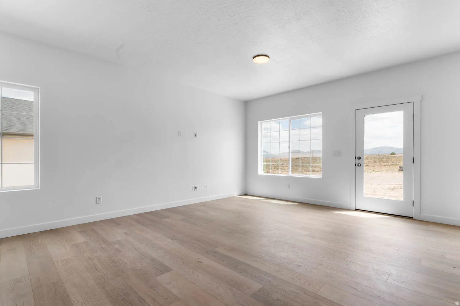Spacious room featuring light wood-finish flooring, white walls, and a contemporary flush-mount ceiling light