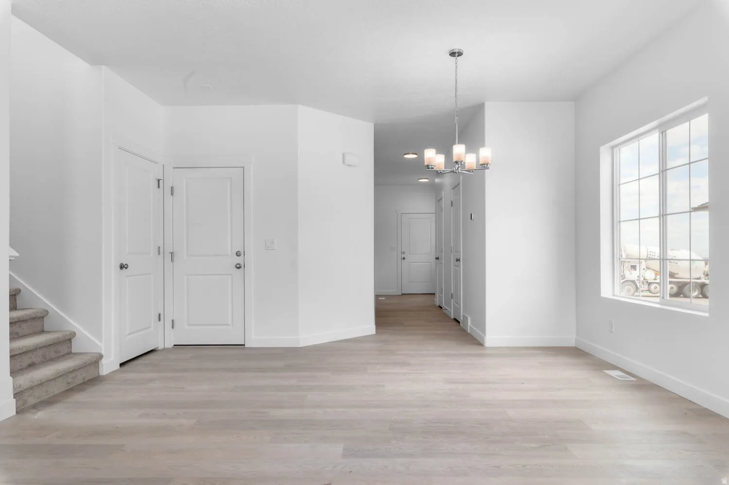 Spacious interior with light wood-finish flooring, white walls, and a contemporary chandelier
