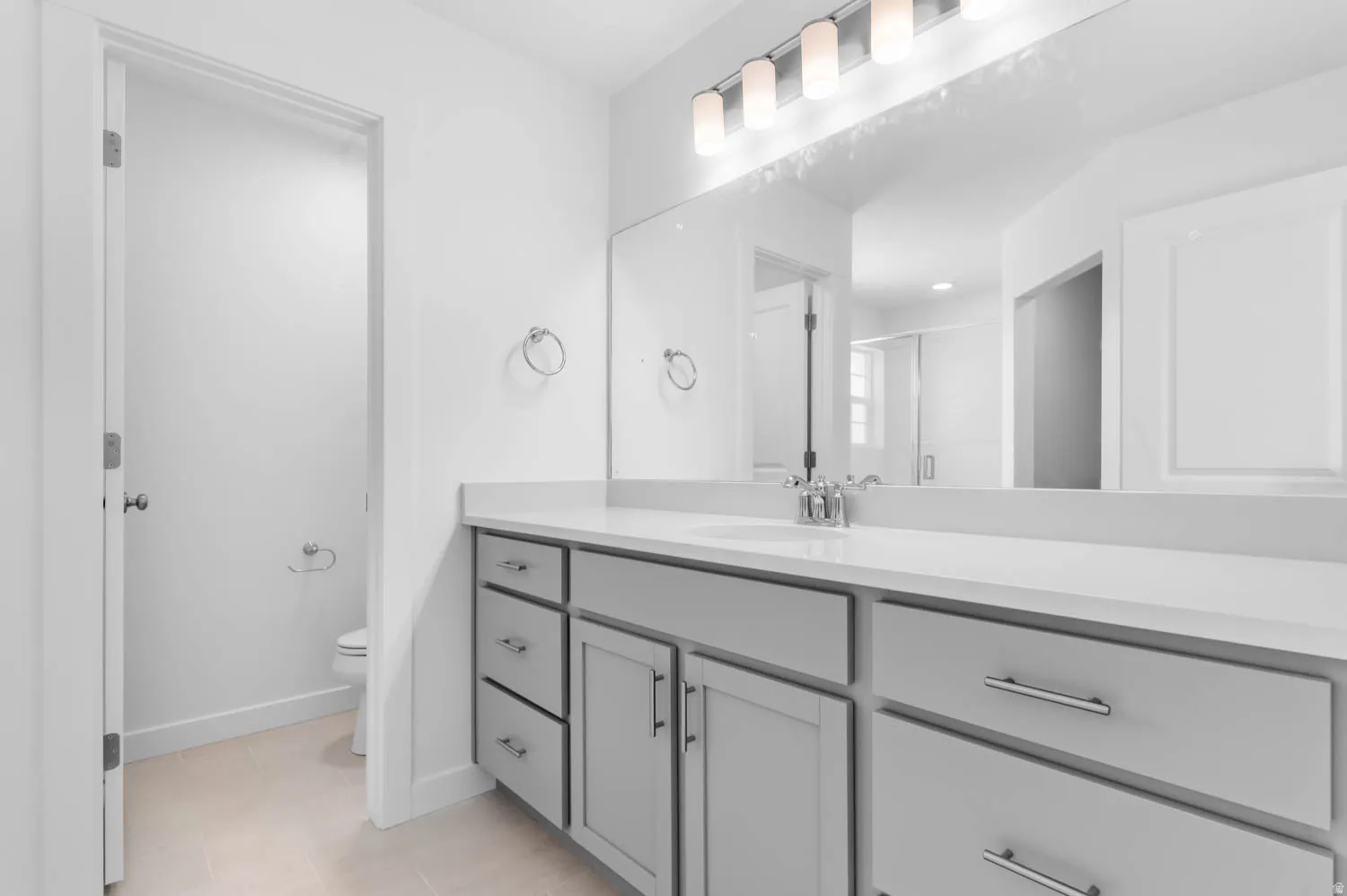 Bathroom vanity featuring a light gray cabinet with brushed nickel hardware, white countertop, and an integrated rectangular sink