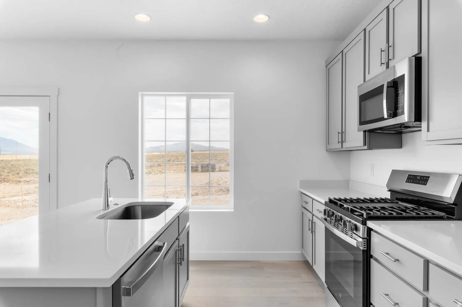 Modern kitchen featuring light gray cabinetry, stainless steel appliances, a center island with an undermount sink, recessed lighting, and wood-finish flooring