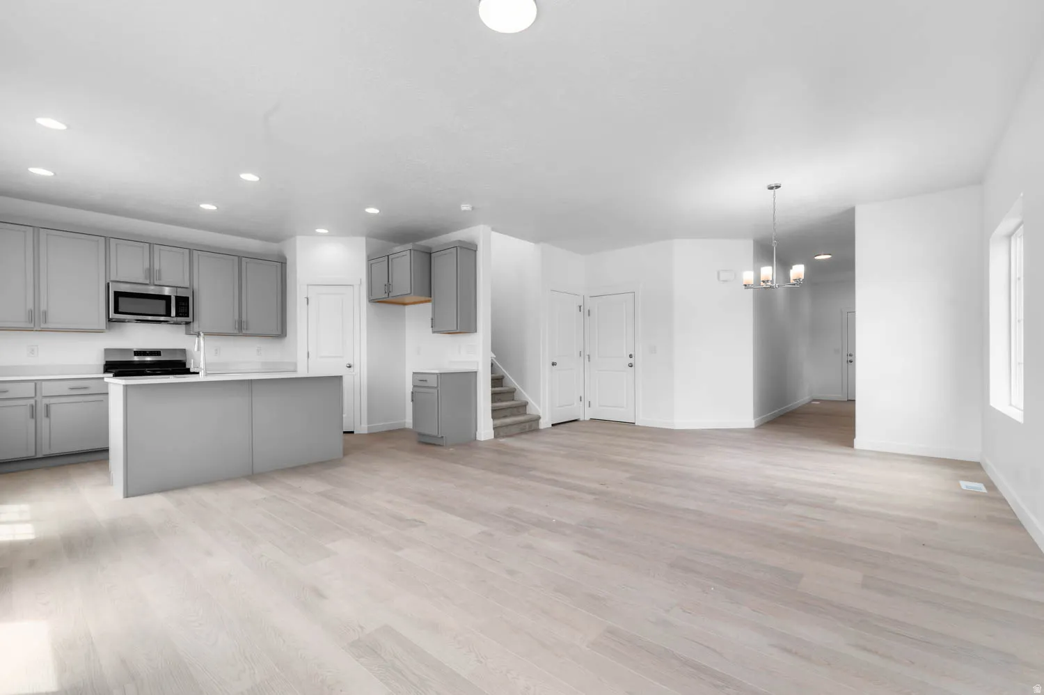 Open-concept living space featuring light wood-finish flooring, recessed lighting, and a modern chandelier