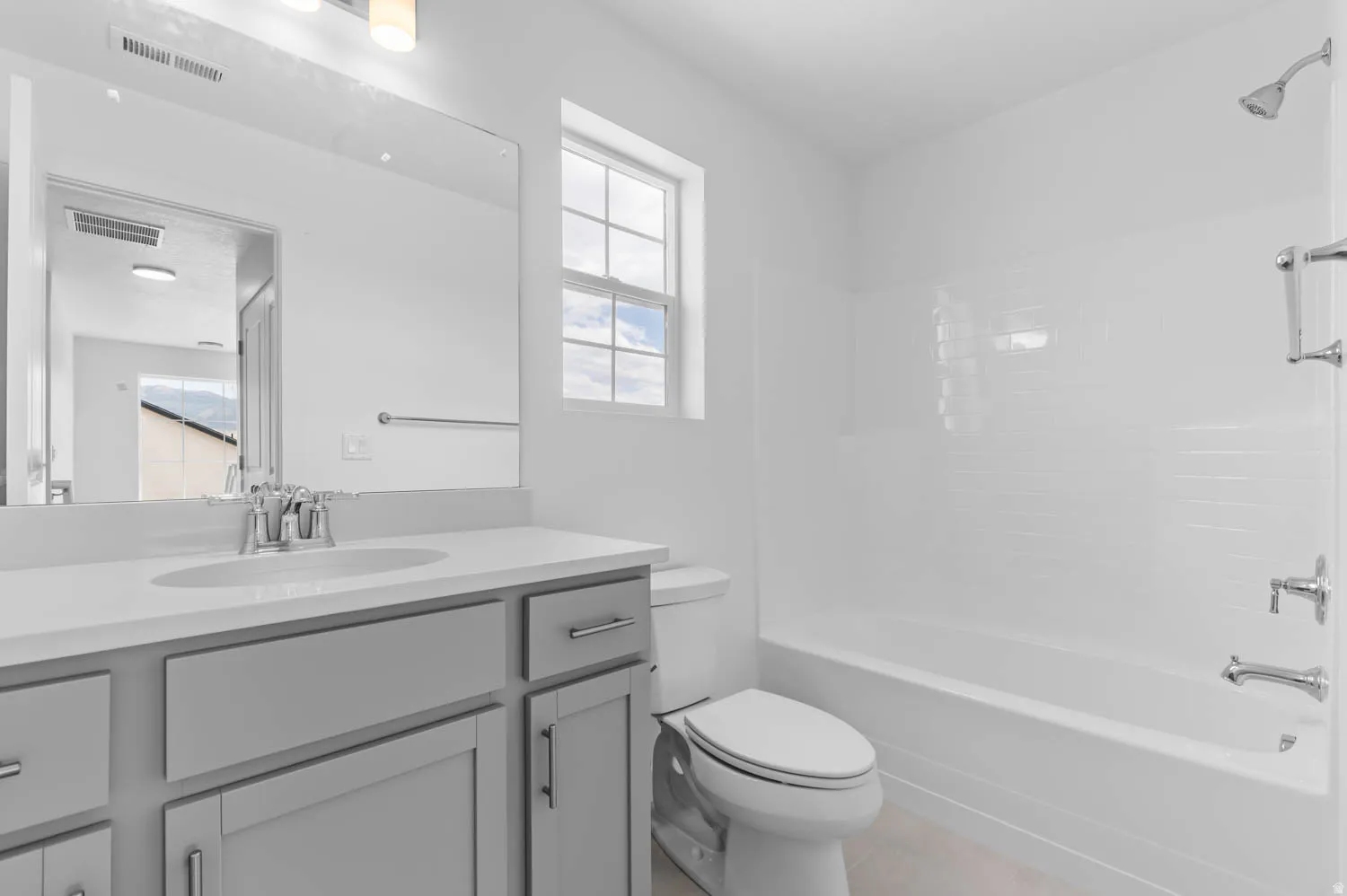 Bathroom featuring a light gray vanity with an integrated sink and chrome fixtures, a large wall-mounted mirror, and an overhead lighting fixture
