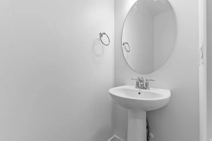 Pedestal sink with chrome fixtures and an oval wall-mounted mirror