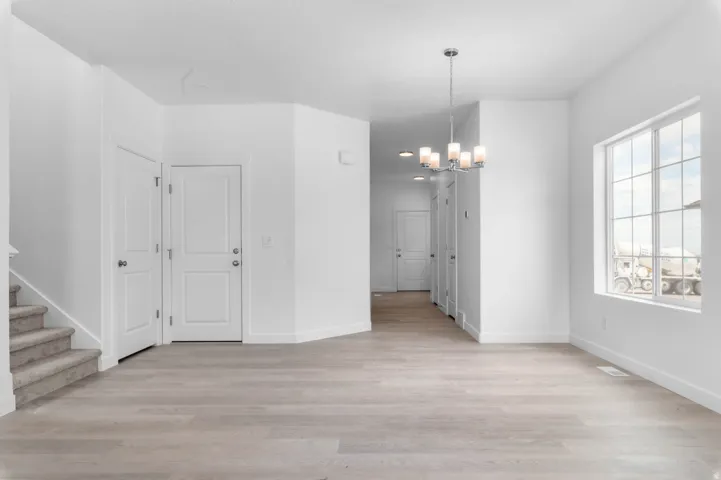 Spacious interior with light wood-finish flooring, white walls, and a contemporary chandelier