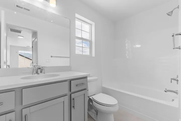 Bathroom featuring a light gray vanity with an integrated sink and chrome fixtures, a large wall-mounted mirror, and an overhead lighting fixture