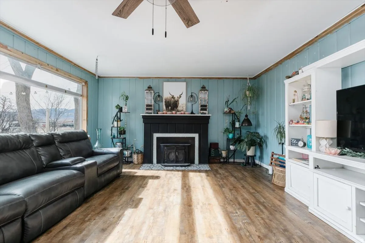 Living area featuring ceiling fan, wood finished floors, ornamental molding, and a fireplace with flush hearth