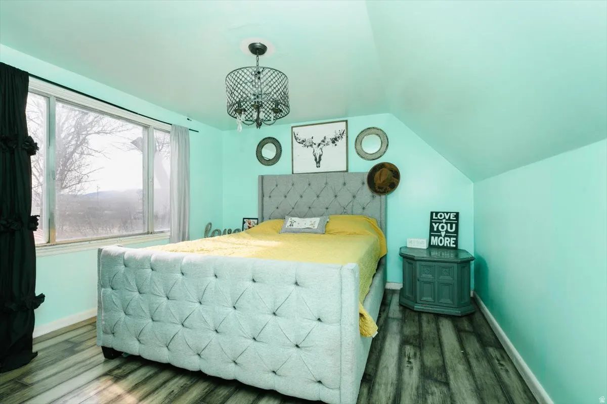 Bedroom with lofted ceiling, dark wood finished floors, and suspended lighting