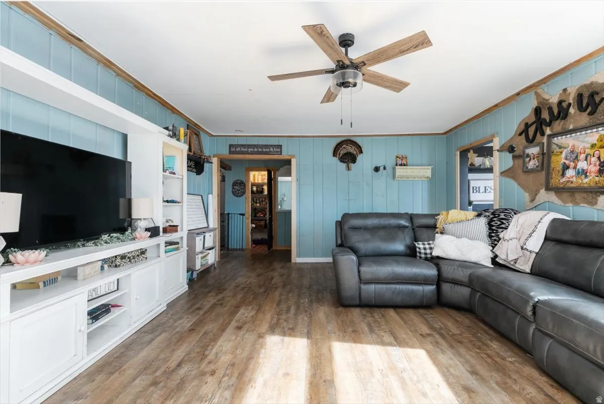 Living area featuring wood finished floors, a ceiling fan, and crown molding