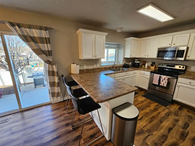 Kitchen featuring white cabinets, appliances with stainless steel finishes, a peninsula, dark wood-style floors, and dark countertops