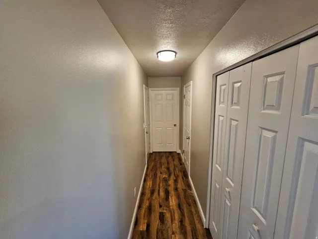 Corridor with a textured ceiling, dark wood-style flooring, and a textured wall