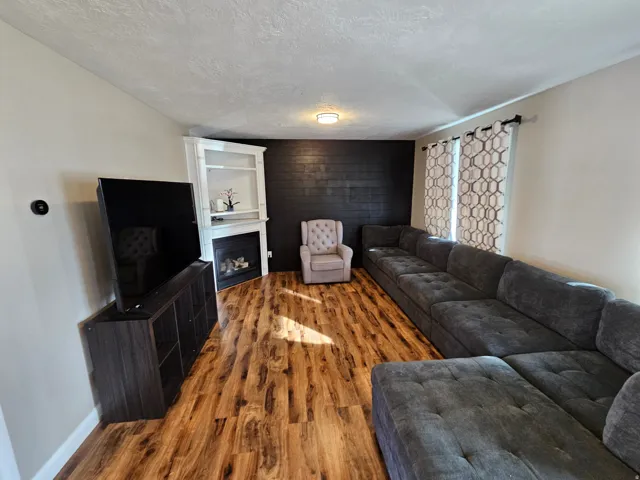 Living room with wood finished floors, a fireplace, a textured ceiling, and an accent wall