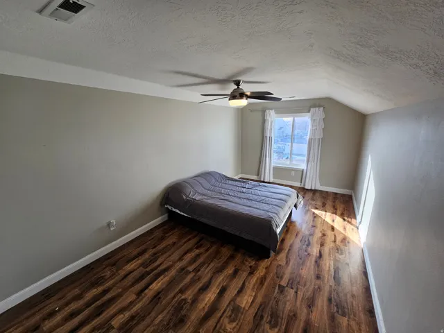 Bedroom with a textured ceiling, dark wood-style flooring, lofted ceiling, and ceiling fan