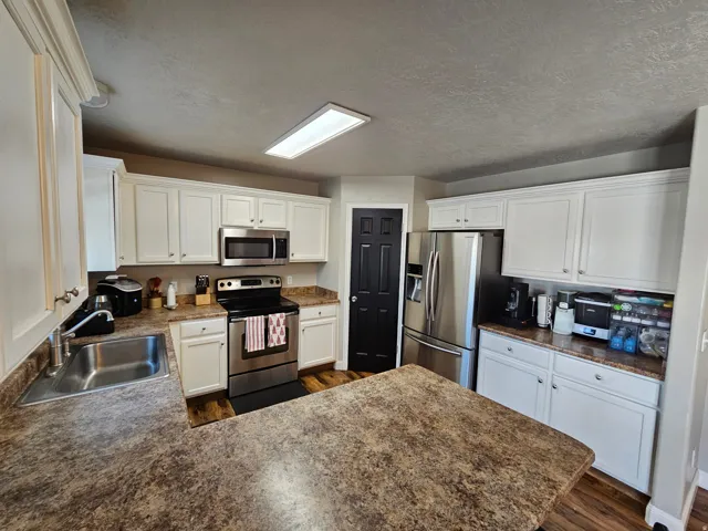 Kitchen featuring appliances with stainless steel finishes, a peninsula, white cabinetry, dark countertops, and a textured ceiling