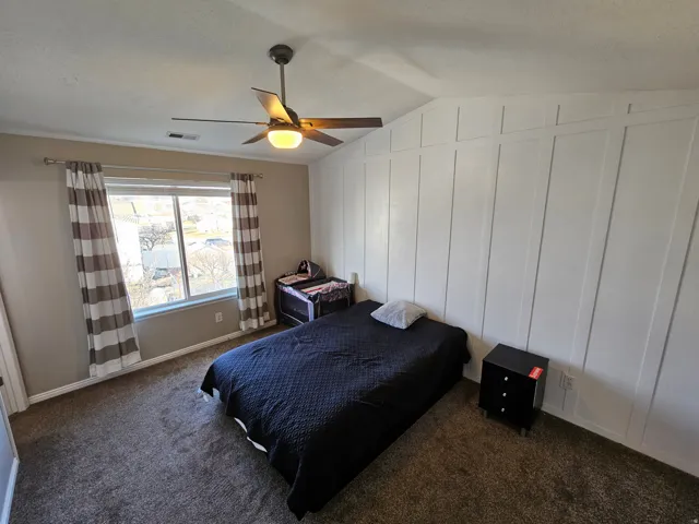 Bedroom featuring lofted ceiling, dark carpet, a ceiling fan, and a decorative wall