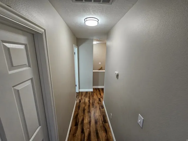 Hall featuring a textured ceiling, dark wood-style flooring, and a textured wall