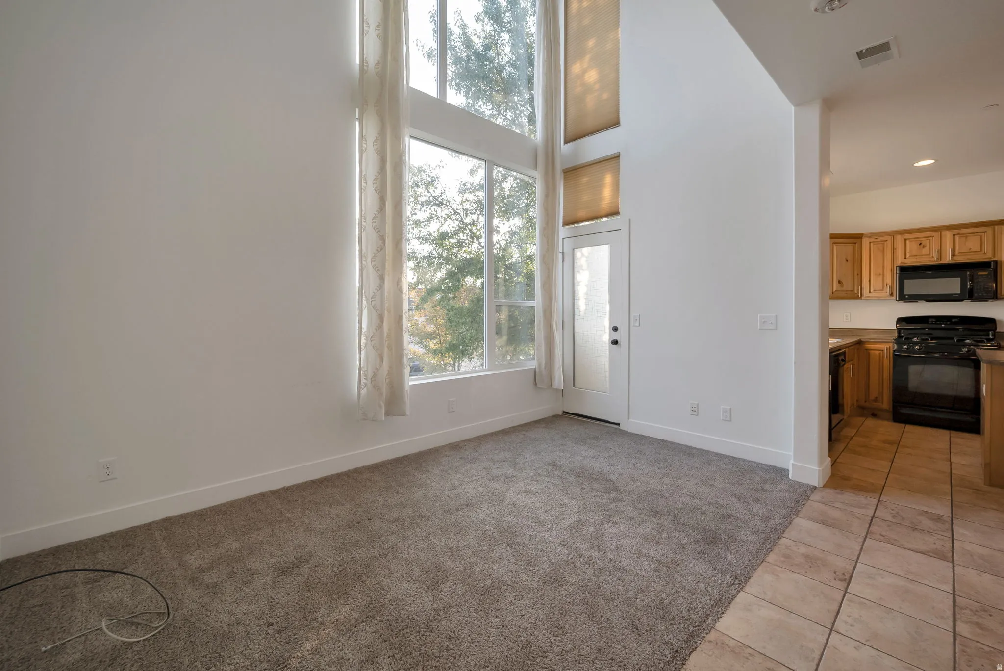 Unfurnished living room featuring light colored carpet, a towering ceiling, and light tile patterned floors