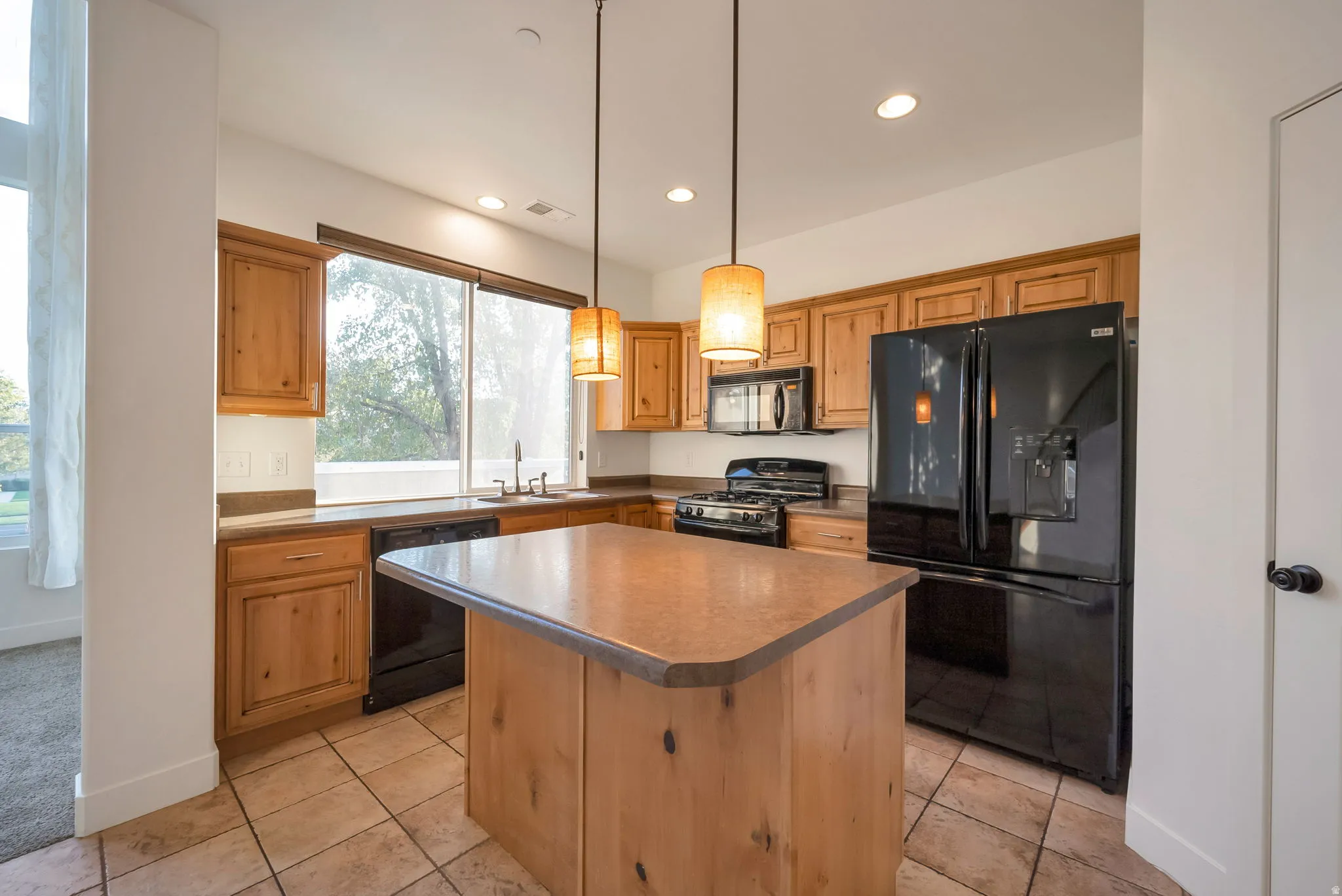 Kitchen featuring a kitchen island, black appliances, decorative light fixtures, light tile patterned floors, and recessed lighting