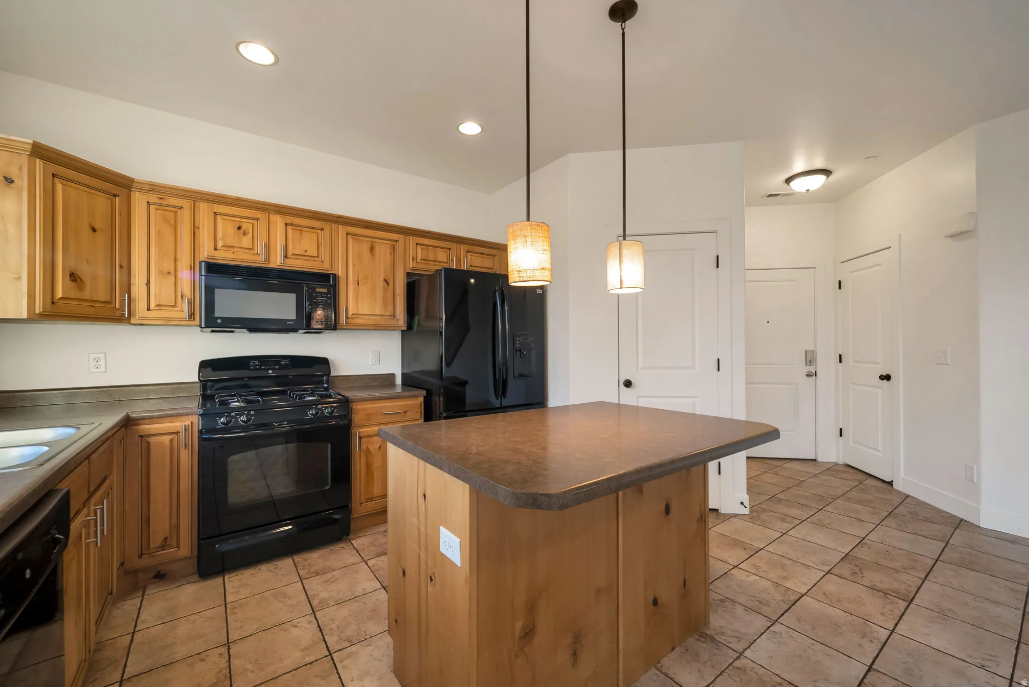 Kitchen featuring black appliances, a center island, dark countertops, pendant lighting, and brown cabinetry