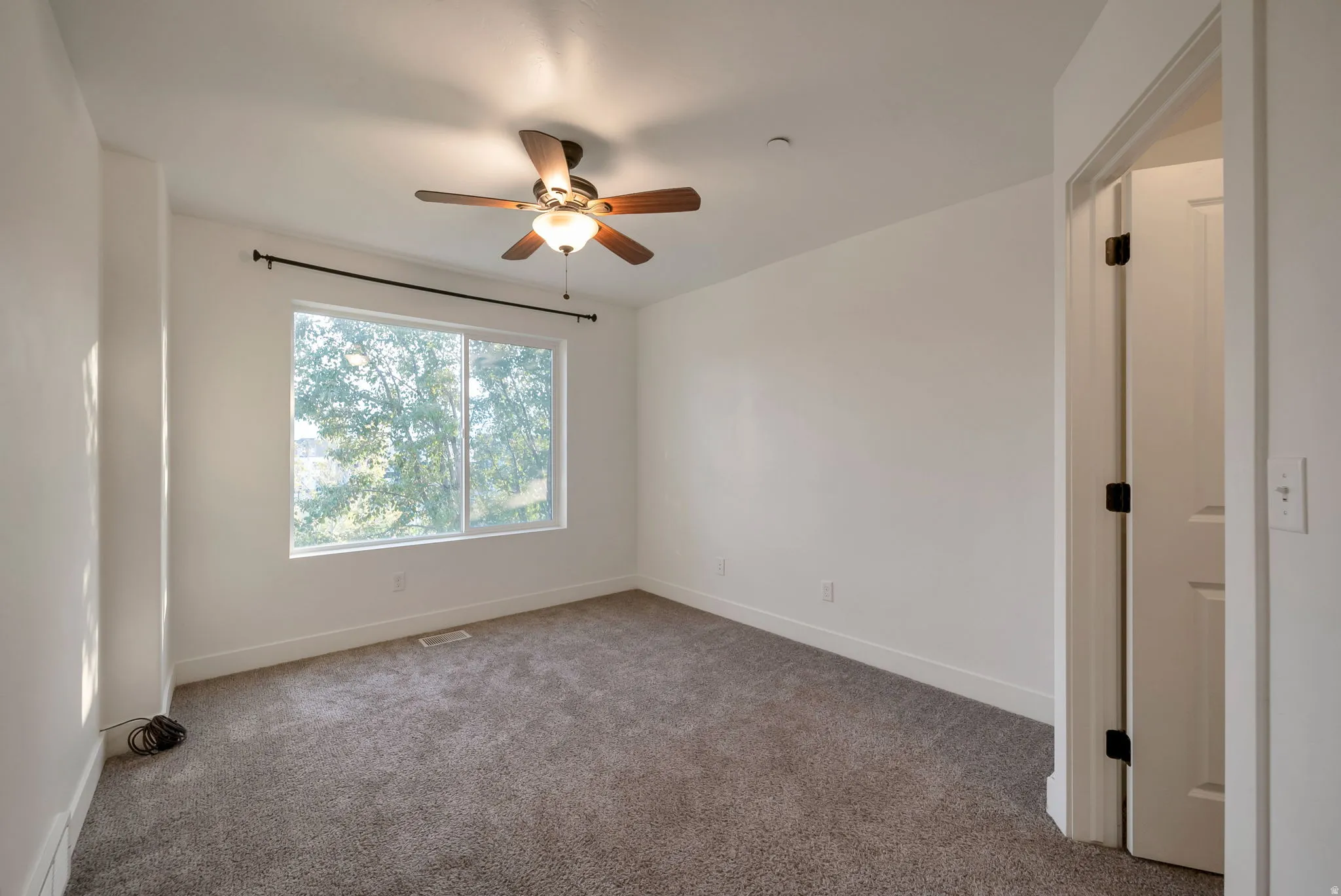 Empty room featuring light colored carpet and a ceiling fan