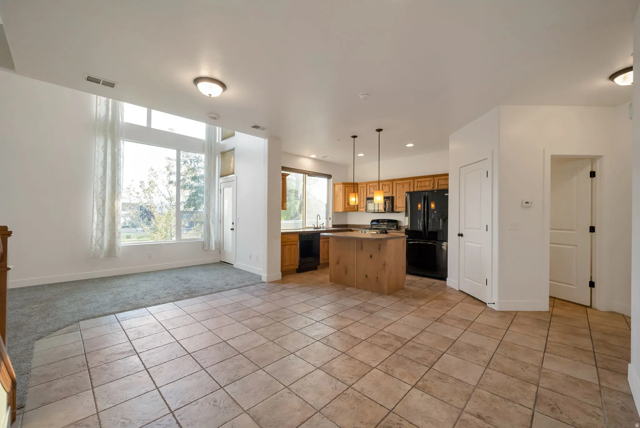 Kitchen with open floor plan, a kitchen island, hanging light fixtures, black appliances, and light tile patterned floors