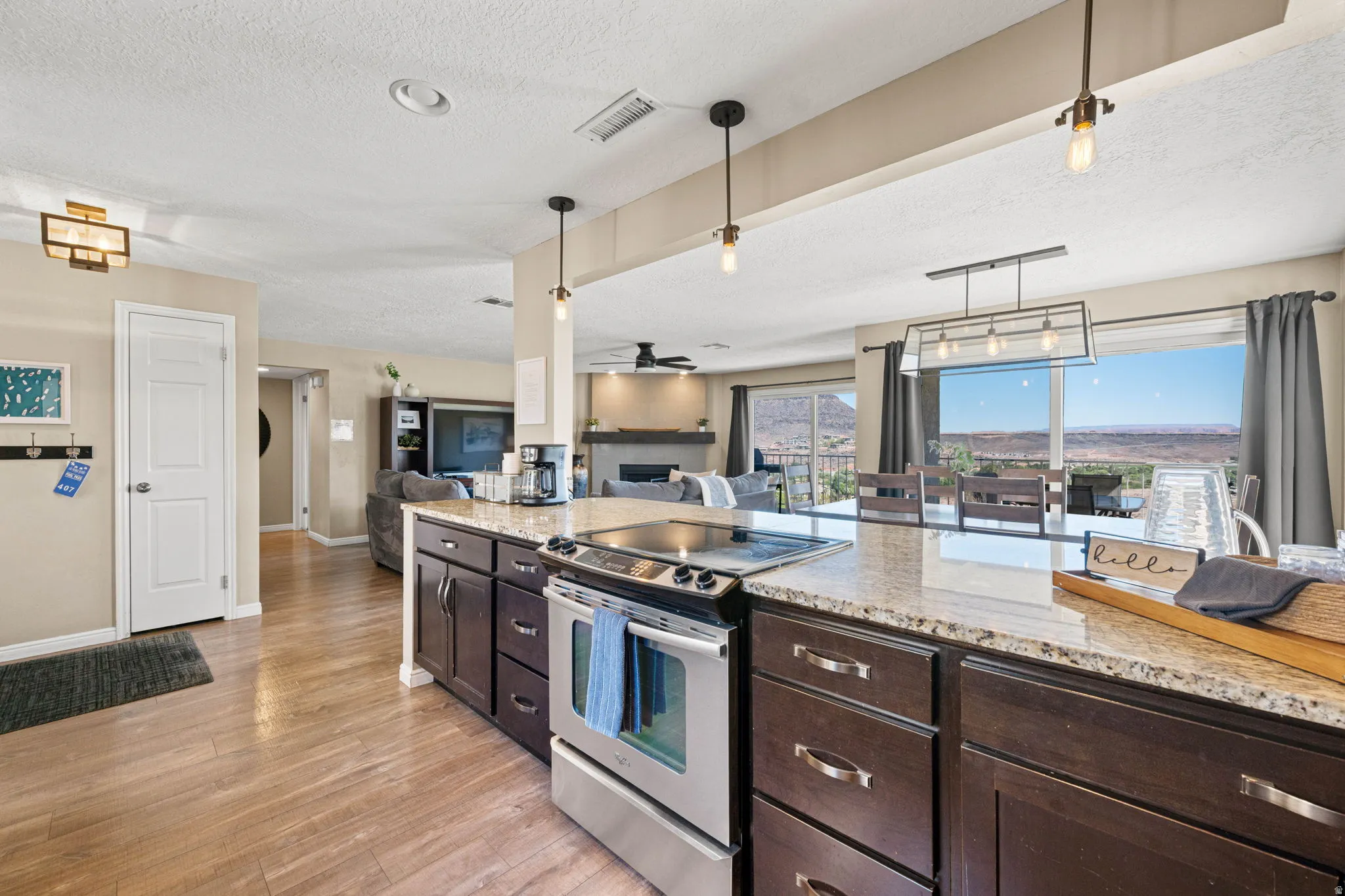 Kitchen with dark brown cabinets, stainless steel range with electric cooktop, a textured ceiling, open floor plan, and a fireplace