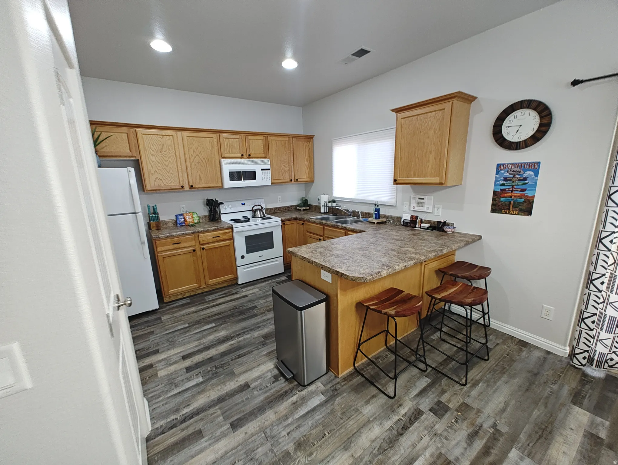 Kitchen with a peninsula, white appliances, a kitchen breakfast bar, dark wood-style floors, and brown cabinetry