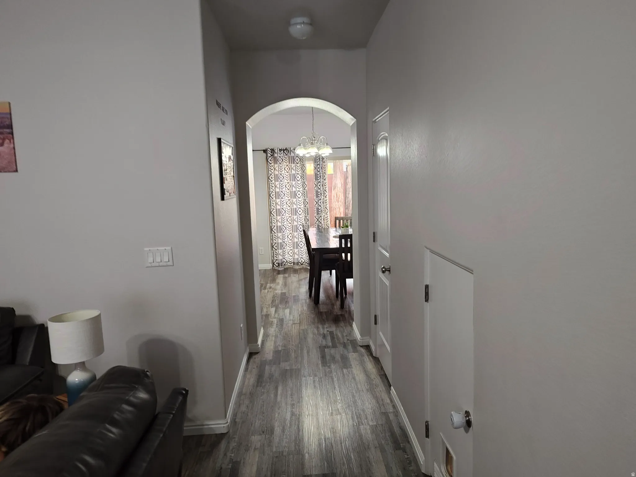 Hallway featuring arched walkways, dark wood finished floors, and hanging lights