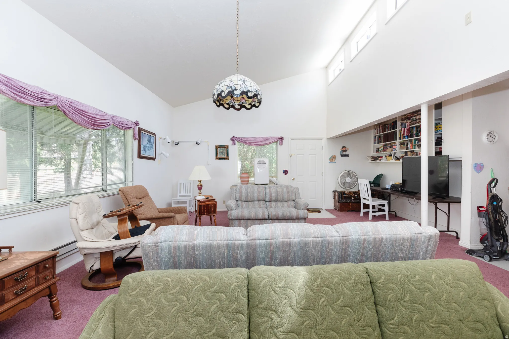 Carpeted living room featuring a desk, high vaulted ceiling, and a baseboard heating unit