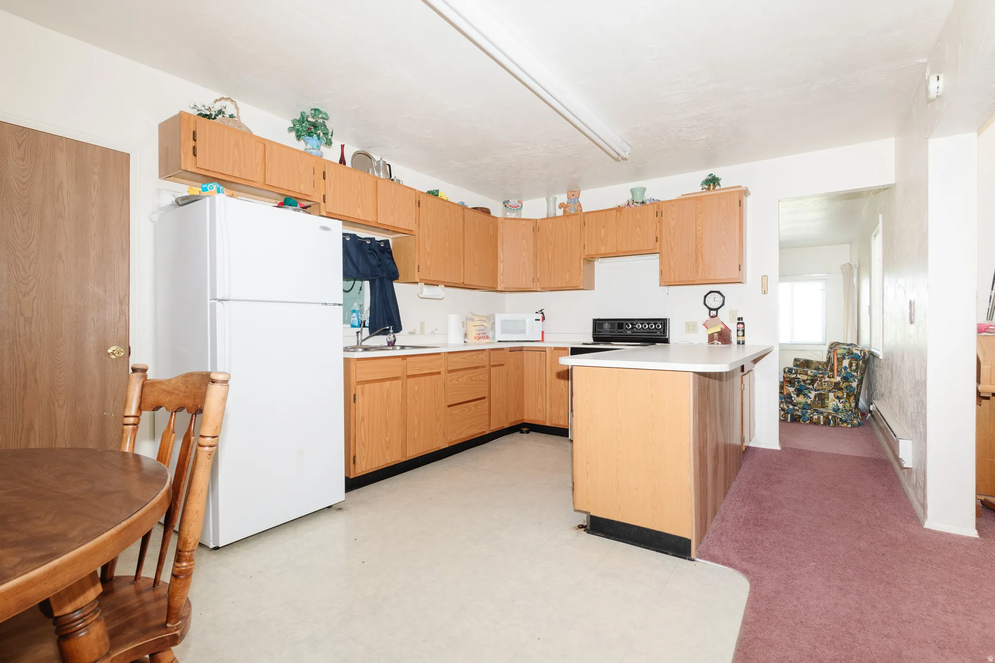 Kitchen featuring a peninsula, white appliances, light countertops, light floors, and a baseboard radiator