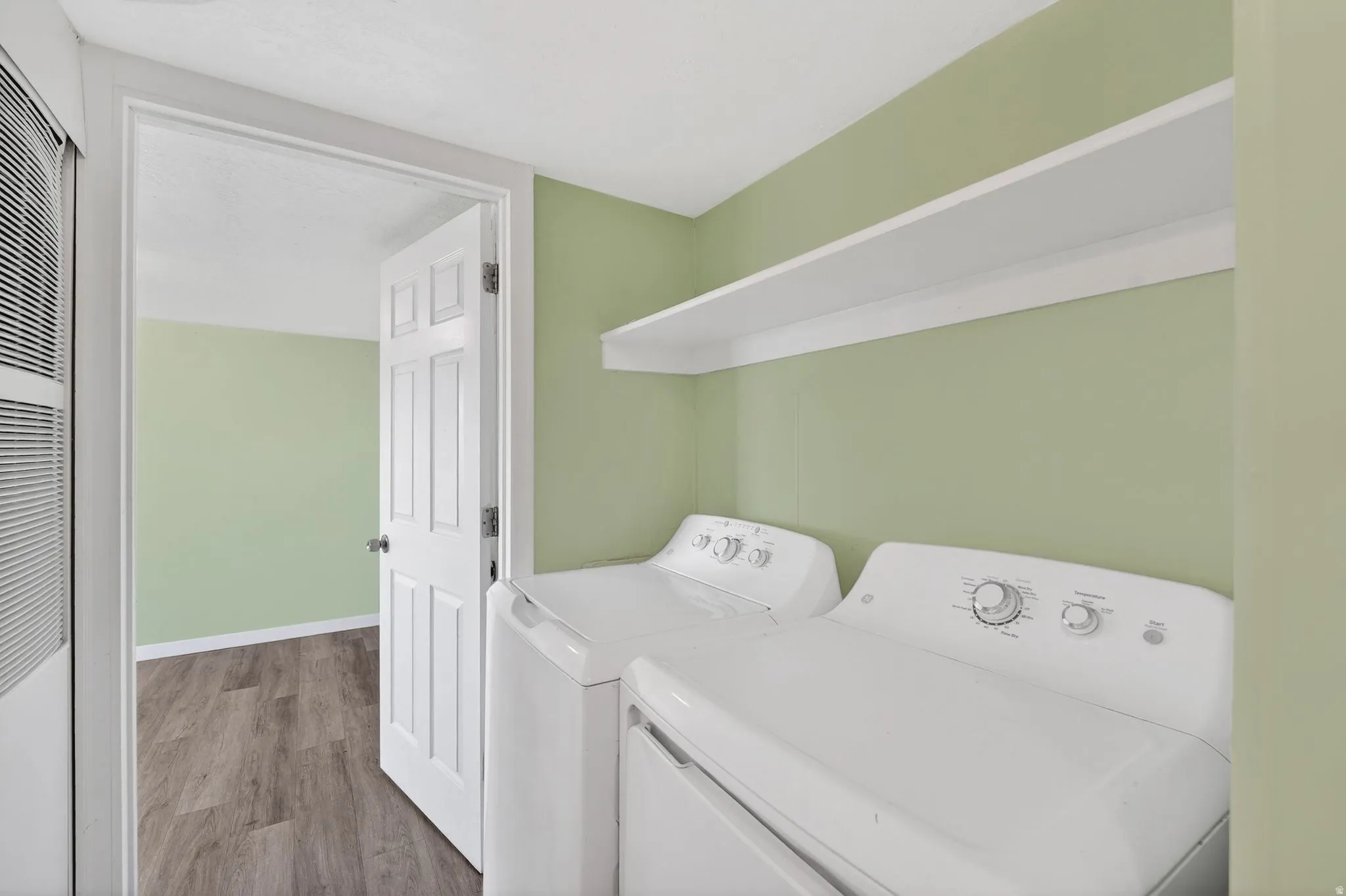 Washroom with wood finished floors, washing machine and clothes dryer, and a heating unit
