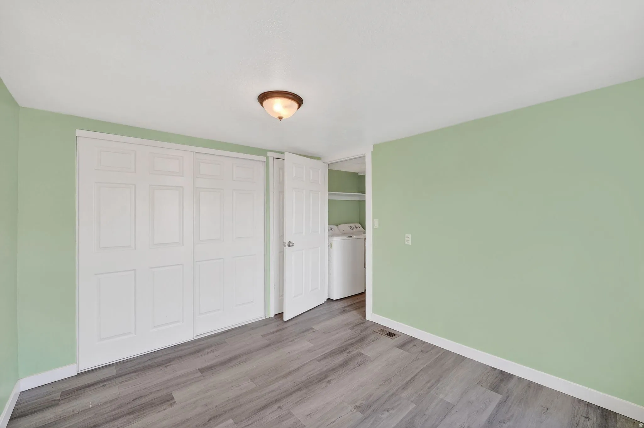 Unfurnished bedroom with wood finished floors, a closet, and washing machine and dryer