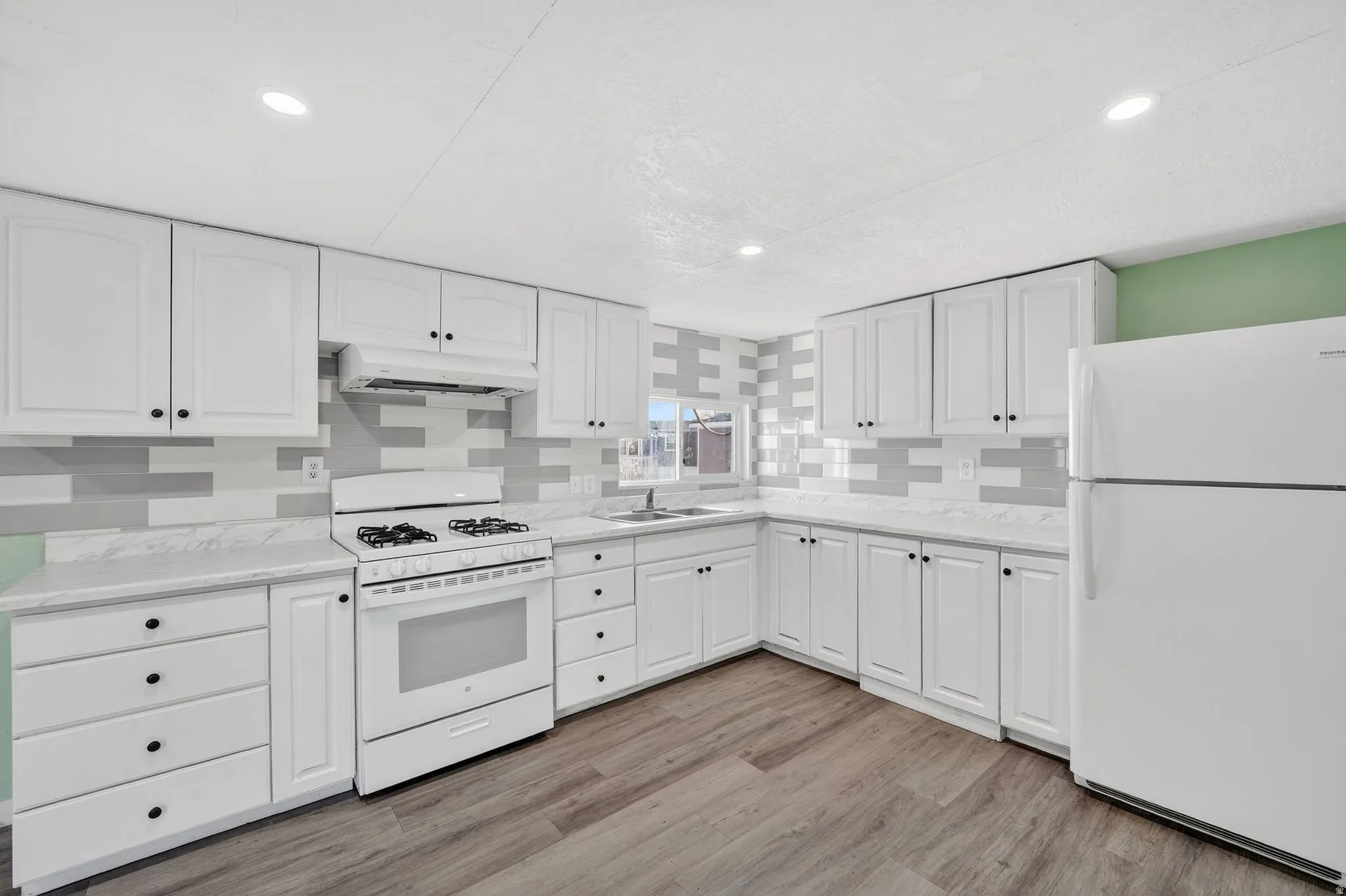Kitchen with white appliances, white cabinetry, light countertops, under cabinet range hood, and light wood finished floors
