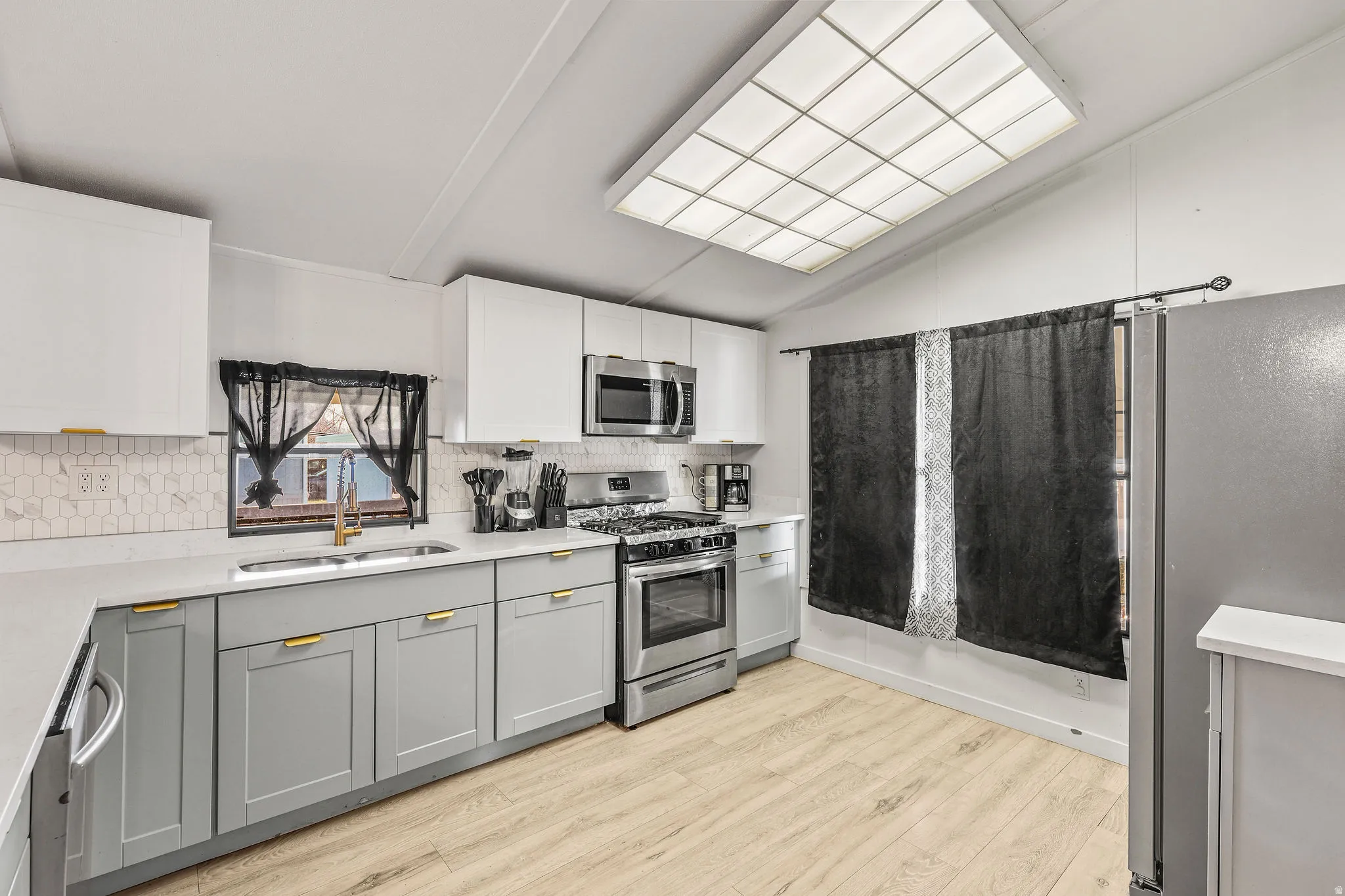 Kitchen featuring stainless steel appliances, gray cabinetry, vaulted ceiling, tasteful backsplash, and light wood finished floors