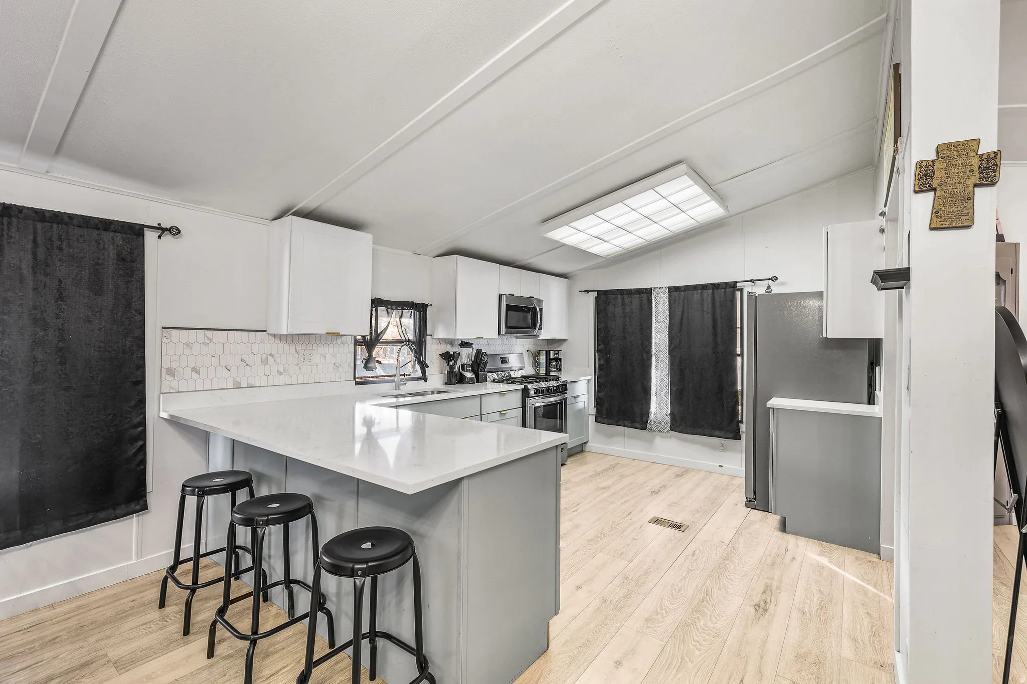 Kitchen with lofted ceiling, light wood finished floors, white cabinetry, a peninsula, and a breakfast bar area