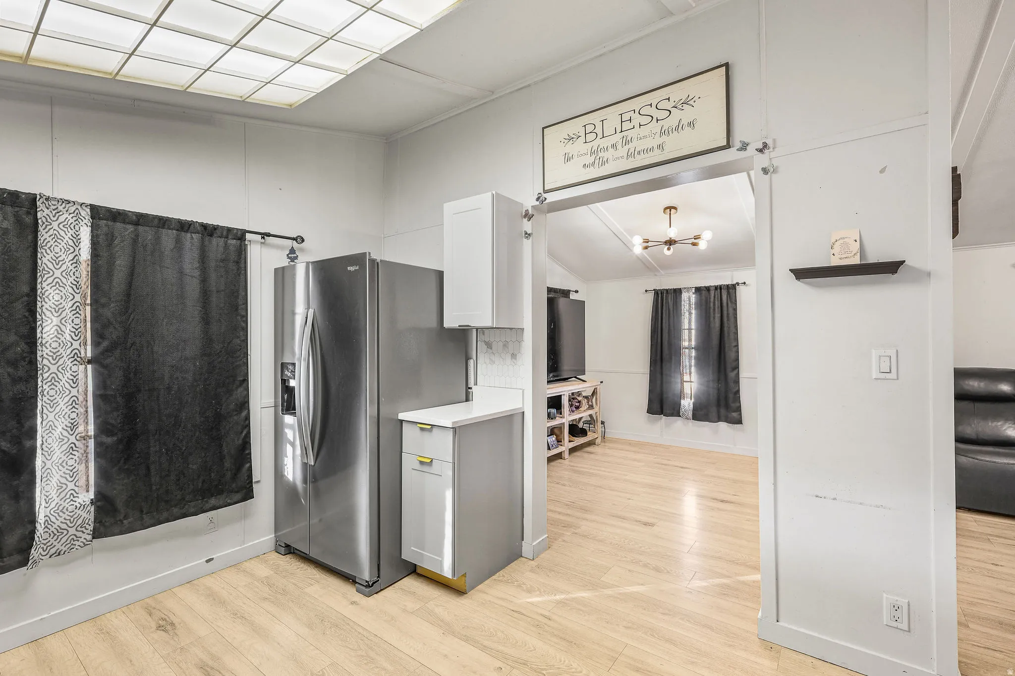 Kitchen featuring stainless steel refrigerator with ice dispenser, light countertops, a chandelier, and light wood-type flooring