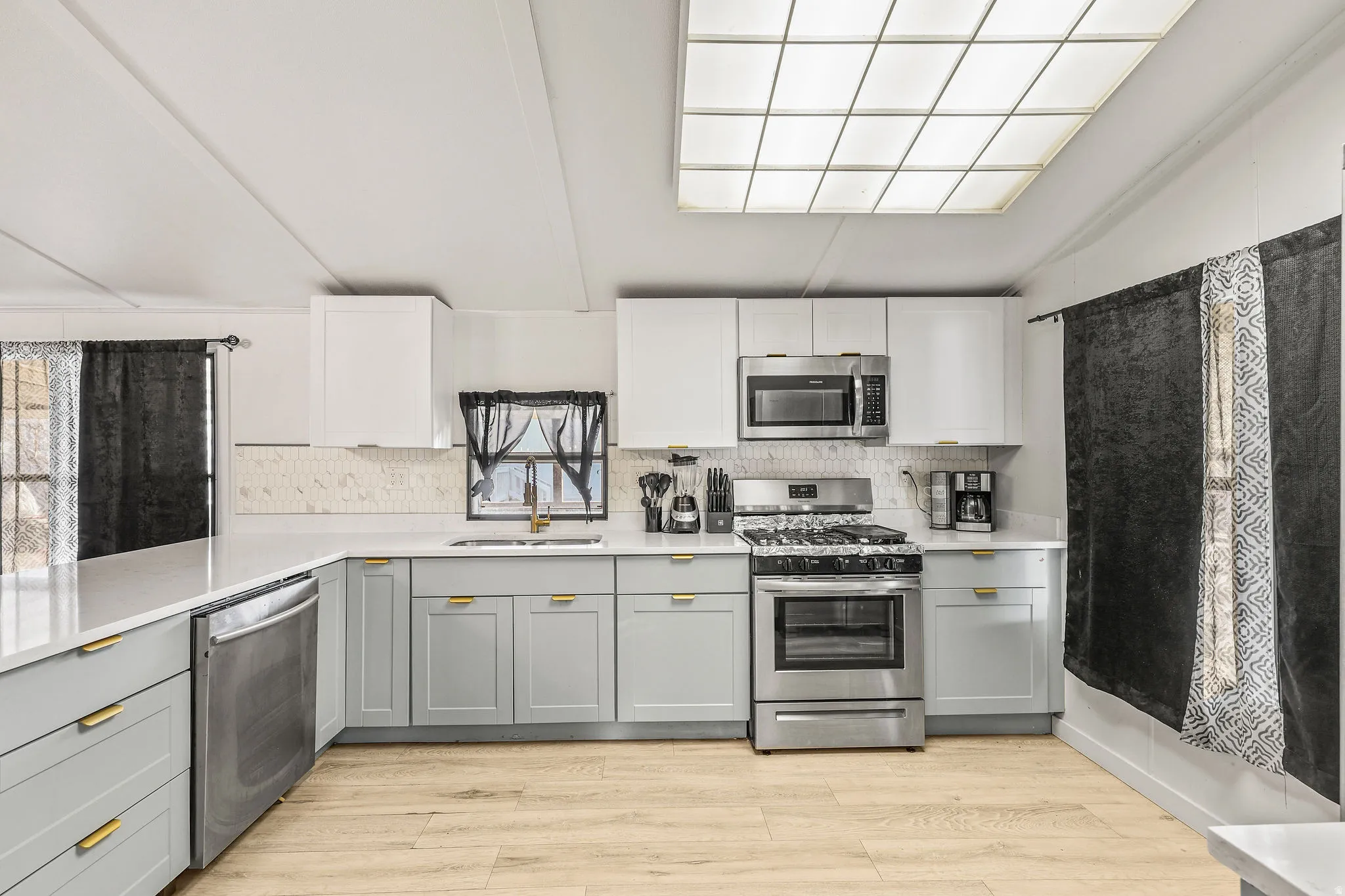 Kitchen with gray cabinets, appliances with stainless steel finishes, white cabinets, decorative backsplash, and vaulted ceiling