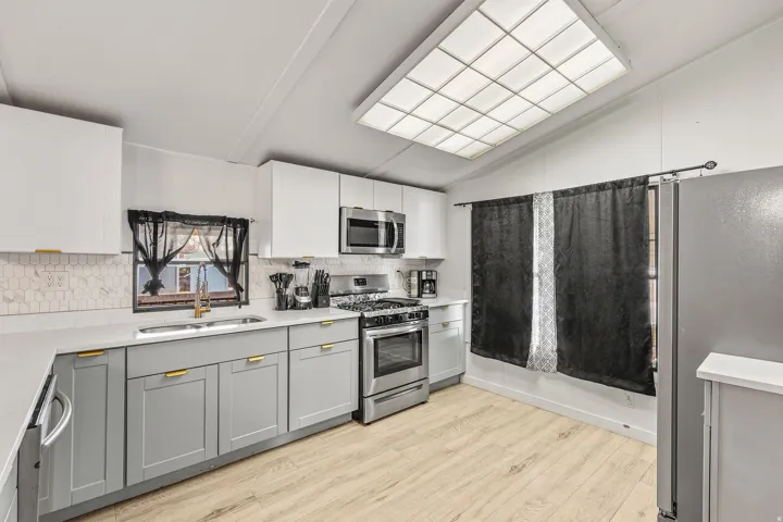 Kitchen featuring stainless steel appliances, gray cabinetry, vaulted ceiling, tasteful backsplash, and light wood finished floors