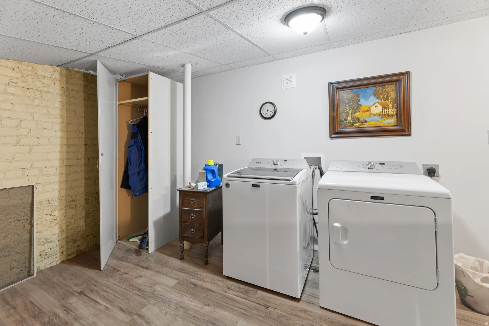 Washroom featuring brick wall, light wood-style floors, a drop ceiling, and independent washer and dryer