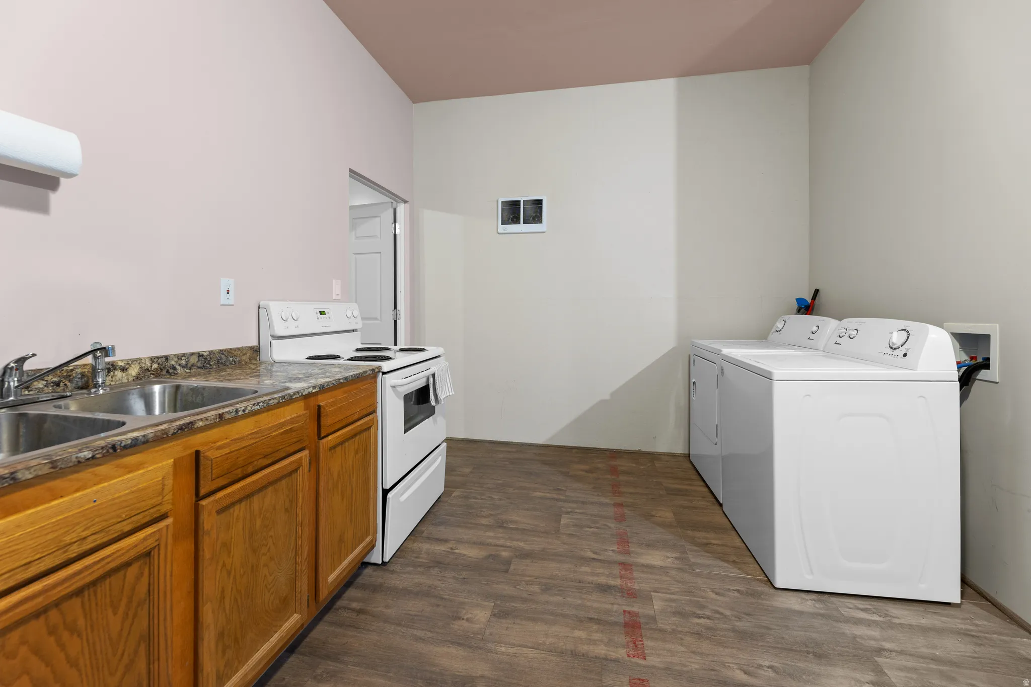 Kitchen with electric range, brown cabinetry, dark wood-style floors, and washing machine and dryer