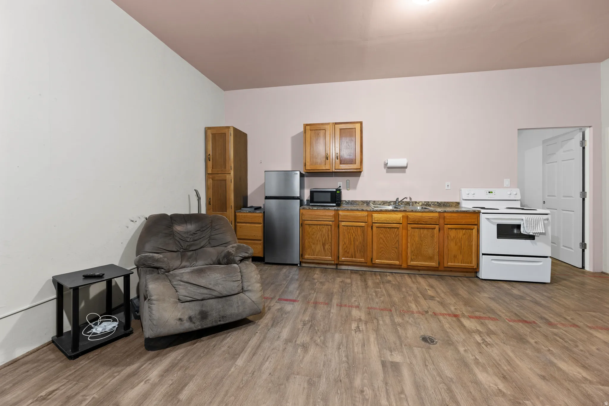 Kitchen featuring white range with electric stovetop, brown cabinetry, dark wood-type flooring, freestanding refrigerator, and open floor plan