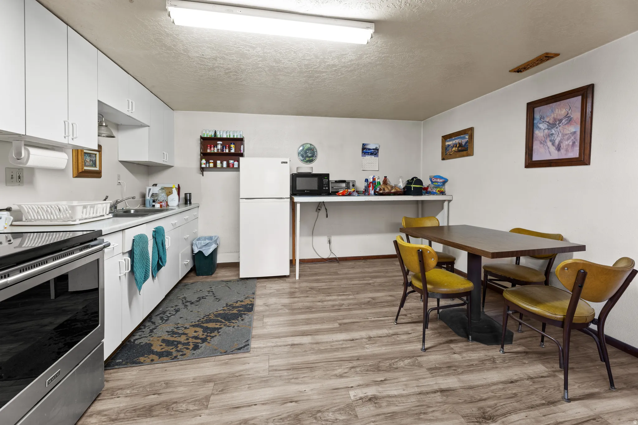 Kitchen with electric range, white cabinets, light countertops, a textured ceiling, and freestanding refrigerator