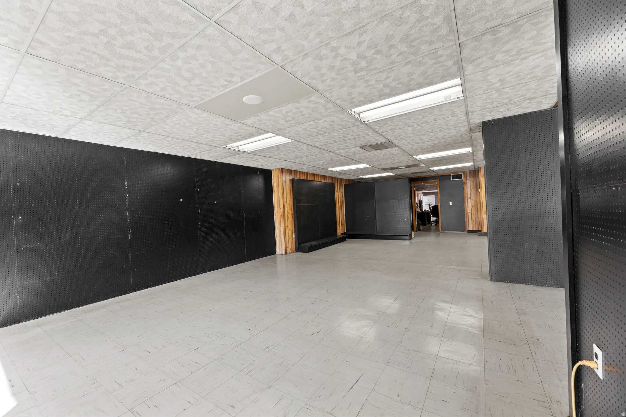 Empty room featuring light flooring, wood walls, and a drop ceiling