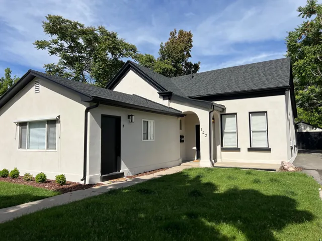 View of front of house featuring stucco siding, a front yard, and a shingled roof