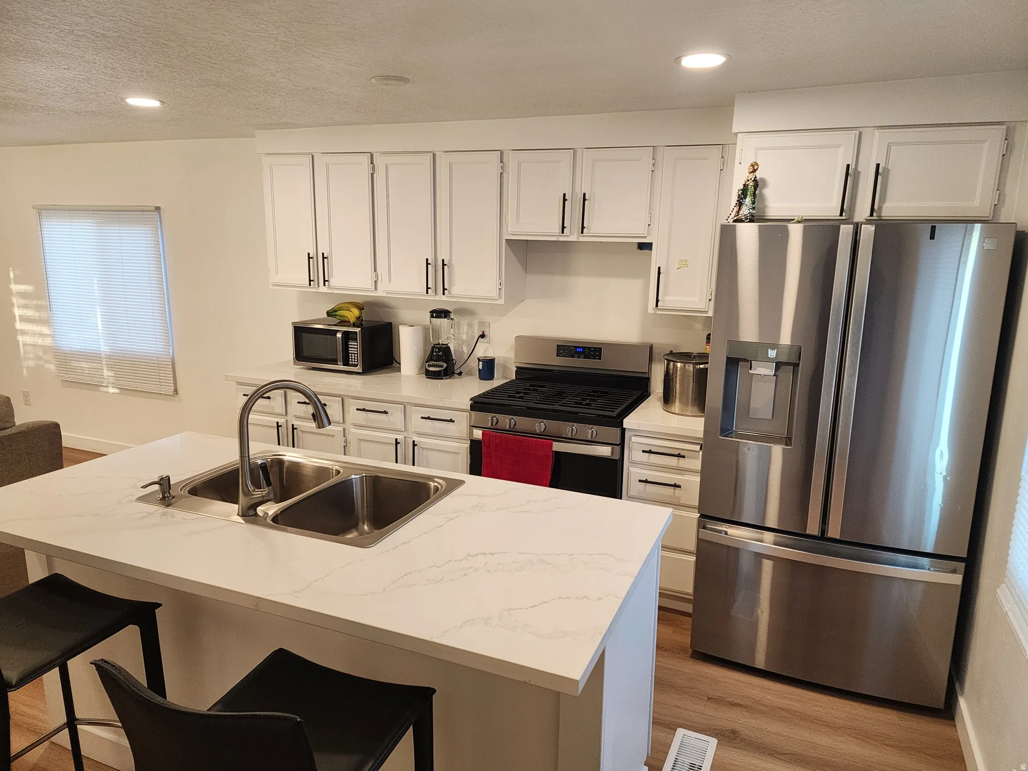 Kitchen with stainless steel appliances, light countertops, white cabinetry, light wood-style floors, and a textured ceiling