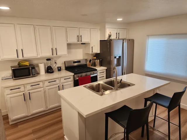 Kitchen with a breakfast bar, stainless steel appliances, white cabinets, a center island with sink, and a textured ceiling