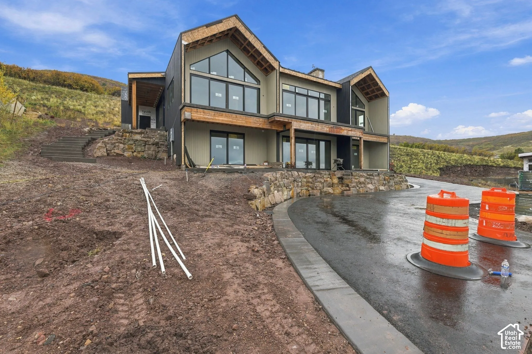 Modern multi-gabled exterior featuring dark metal siding, wood-trimmed rooflines, floor-to-ceiling windows, and integrated natural stone retaining walls