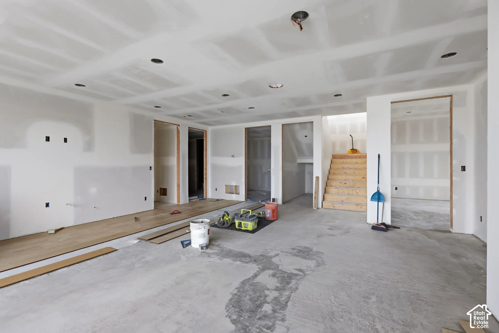 Open-concept interior featuring recessed lighting, unfinished drywall, wood-finish flooring, and a wooden staircase