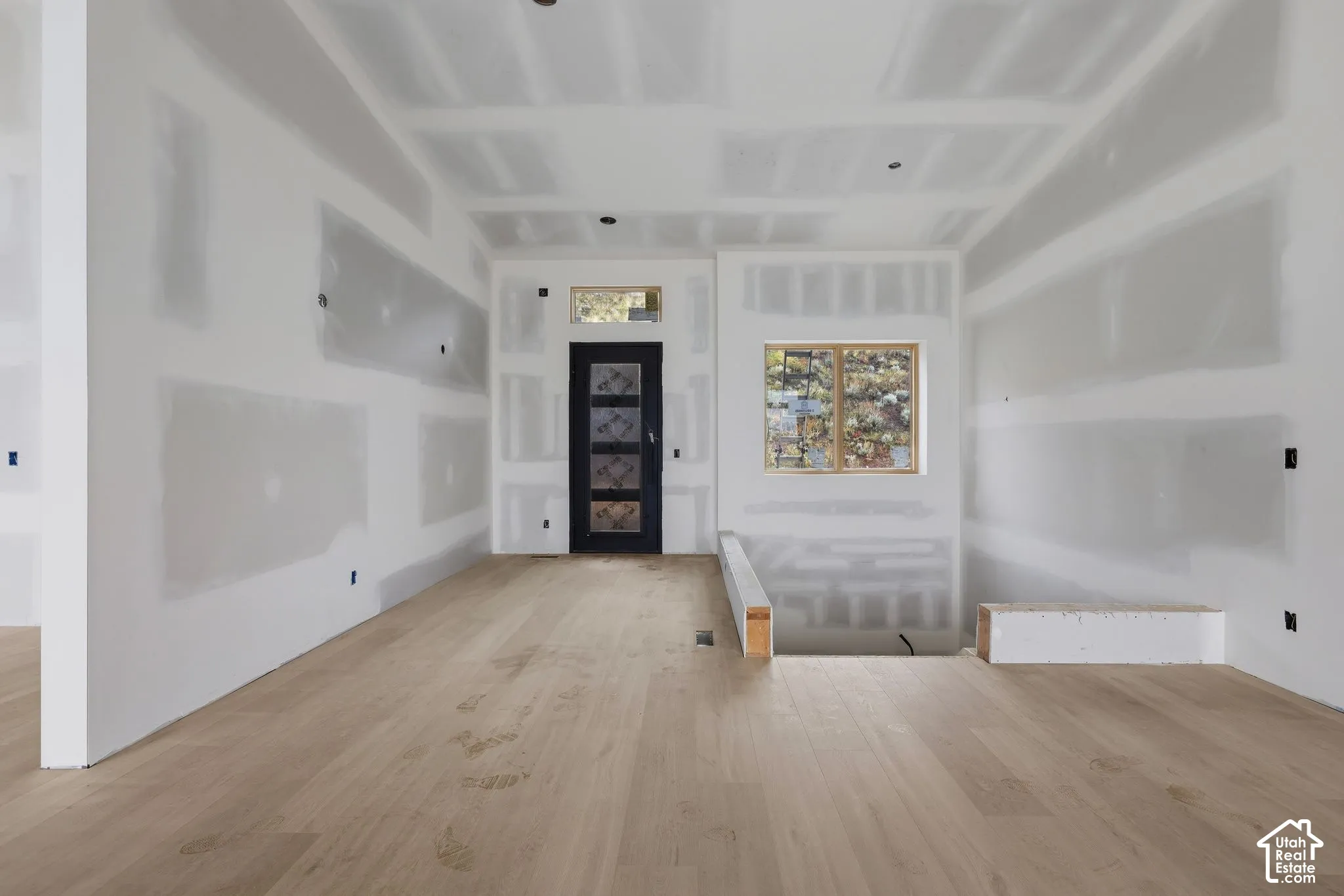 Light-toned wood-finish flooring, entry door with decorative glass inlay, transom window, and dual-pane window